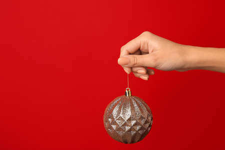 Female hand with shiny Christmas ball on red backgroundの写真素材