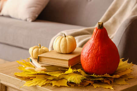 Fresh pumpkins, autumn leaves and books on table in room