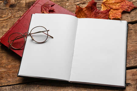 Opened book with blank pages, eyeglasses and autumn leaves on wooden backgroundの写真素材