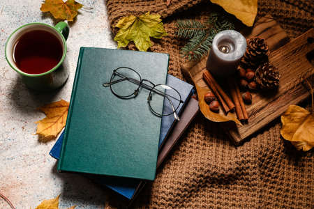 Stack of books, eyeglasses, cup of coffee and autumn decor on table