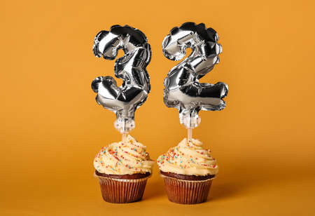 Tasty Birthday cupcakes with number 32 on color background
