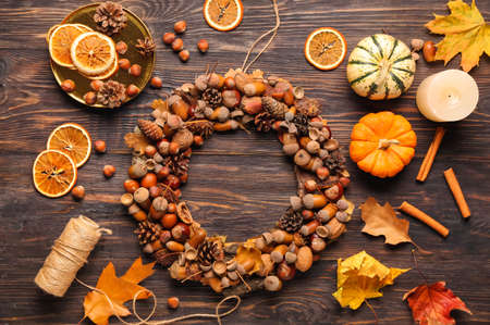 Beautiful acorn wreath, pumpkins, hazelnuts and leaves on dark wooden backgroundの写真素材