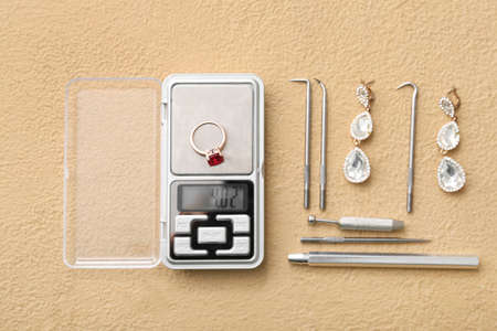 Jewelry scales with ring, earrings and different tools on beige background