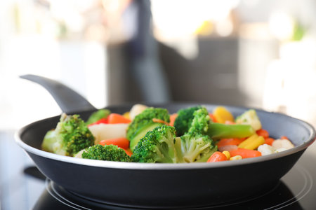 Frying pan with vegetables on electric stove in kitchen, closeupの写真素材