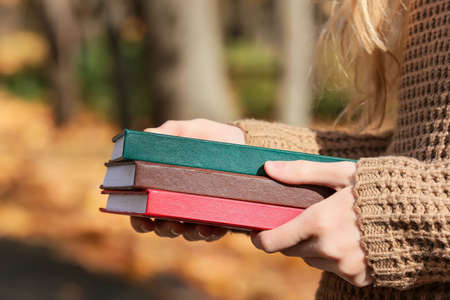 Young woman in warm sweater holding books outdoors, closeupの写真素材