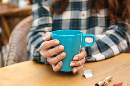 Woman with blue cup of hot tea at table in cafe