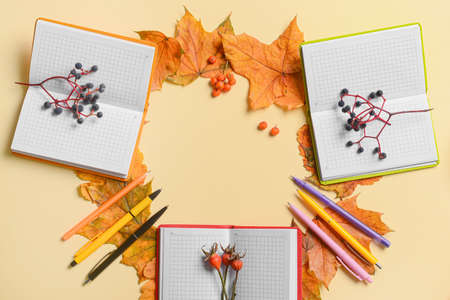 Frame made of notebooks, pens, berries and fallen leaves on beige background