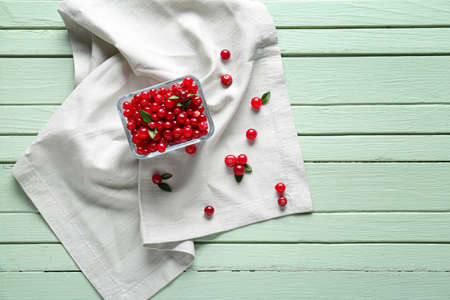 Bowl with ripe lingonberry on color wooden background