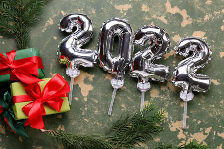 Figure 2022 made of silver balloons, gift boxes and fir tree branches on color background