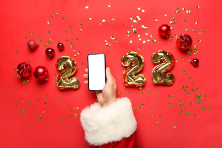 Santa Claus with mobile phone and balloons in shape of figure 2022 on red backgroundの写真素材