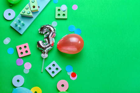 Composition with silver balloon in shape of figure 3 and developmental toys on green background