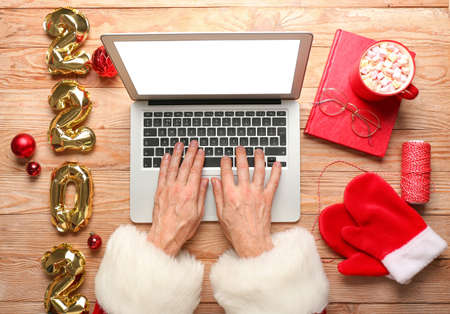 Santa Claus using laptop on wooden background