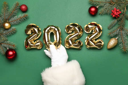 Santa Claus with balloons in shape of figure 2022 and Christmas decor on green background