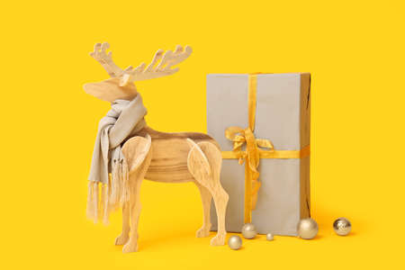 Wooden reindeer with scarf, big Christmas gift and balls on yellow backgroundの写真素材