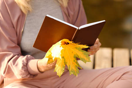 Mature woman reading book near river on autumn day