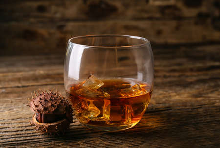 Glass of chestnut whiskey on wooden background