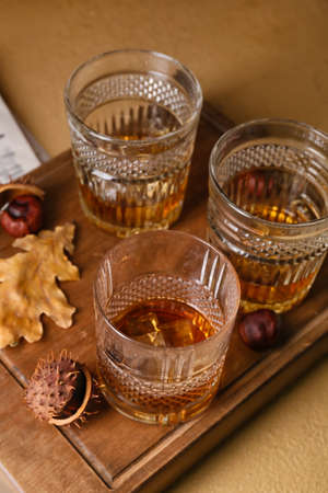 Wooden board with glasses of chestnut whiskey on beige background