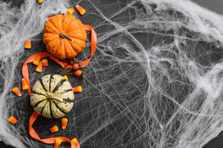 Halloween pumpkins with candies, ribbon and spider's web on black background