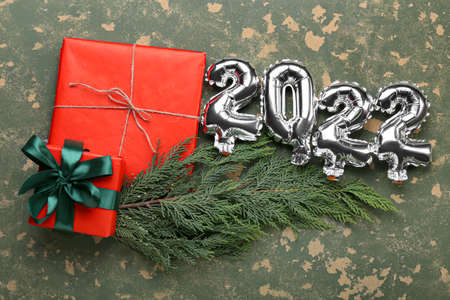 Silver balloons in shape of figure 2022, fir tree branch and Christmas presents on color background