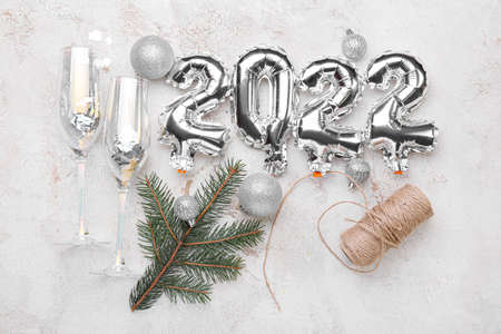 Silver balloons in shape of figure 2022, glasses for champagne and Christmas decor on light...