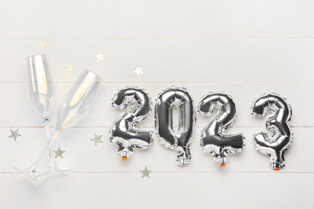 Silver balloons in shape of figure 2023 and glasses for champagne on white wooden backgroundの写真素材