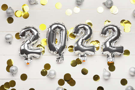 Composition with silver balloons in shape of figure 2022 and Christmas balls on white wooden...