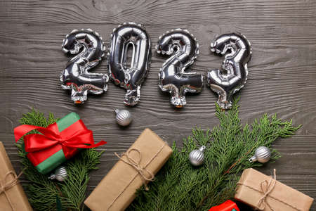 Silver balloons in shape of figure 2023, gift boxes and Christmas decor on dark wooden backgroundの写真素材