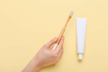 Female hand with wooden toothbrush and paste on color backgroundの写真素材