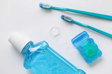 Dental floss with toothbrushes and rinse on white background