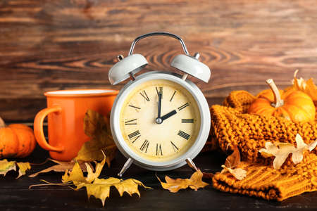 Alarm clock and autumn leaves with cup of tea and clothes on wooden background. daylight saving time endの写真素材