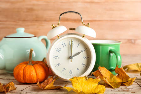 Alarm clock and autumn leaves with tea on wooden background. daylight saving time endの写真素材