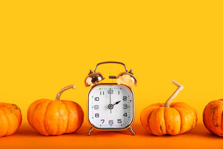 Alarm clock and pumpkins on color background. daylight saving time endの写真素材