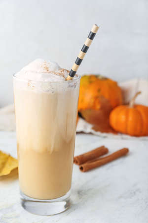 Glass of tasty pumpkin latte on light background