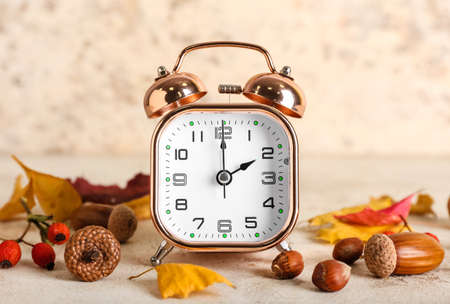 Alarm clock and autumn leaves with nuts on grunge background. daylight saving time end