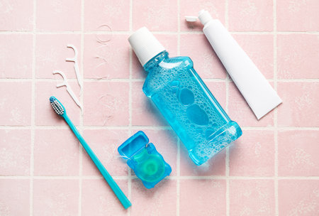 Dental floss with toothpicks, brush, rinse and paste on pink tile background