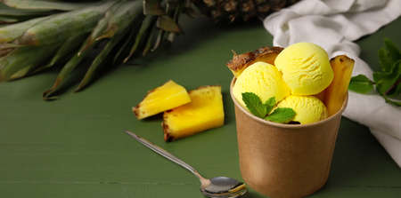 Cup with tasty pineapple ice cream on green wooden background