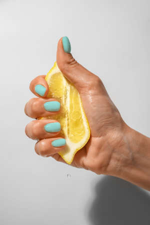 Hand with beautiful mint manicure squeezing lemon on light backgroundの写真素材