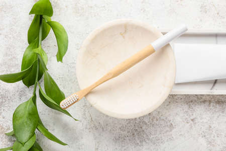 Bowl with bamboo toothbrush and plant branch on grunge backgroundの写真素材