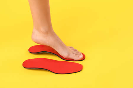 Female foot and red orthopedic insoles on yellow backgroundの写真素材