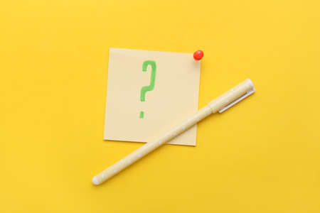 Sticky note with question mark, pin and pen on yellow backgroundの写真素材