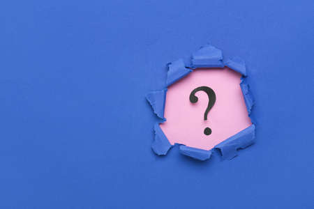Black question mark visible through torn blue paperの写真素材