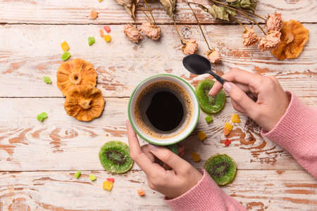 Female hands with cup of coffee, dried fruits and flowers on light wooden background, closeupの写真素材