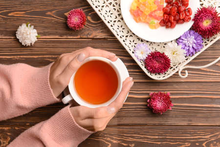 Female hands with cup of tea, sweets and aster flowers on wooden background, closeupの写真素材