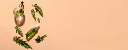 Bottles of cosmetic serum and fern leaves on beige background with space for textの写真素材