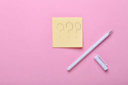 Sticky note with question marks and pen on pink backgroundの写真素材