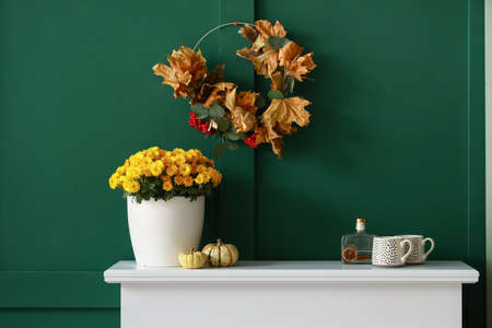 Vase with flowers, pumpkins and cups on mantelpiece near green wallの写真素材