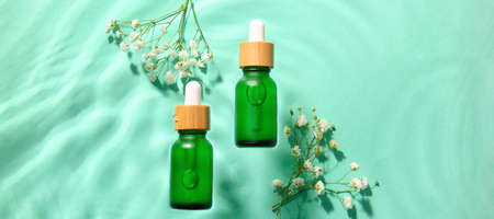 Bottles of cosmetic serum and flowers in water on color backgroundの写真素材