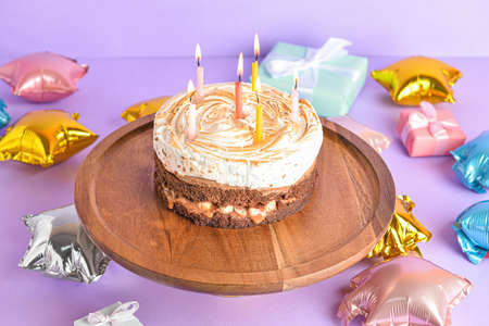 Stand with tasty birthday cake and balloons on purple background
