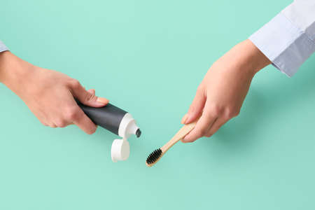 Woman applying black tooth paste onto bamboo brush on blue background, closeupの写真素材
