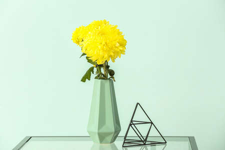 Vase with yellow chrysanthemum flowers on table against blue wallの写真素材